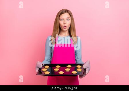 Portrait of attractive trendy funny amazed girl holding tray fresh baked cookies isolated over pink pastel color background Stock Photo