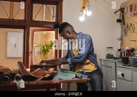 African american young craftsman using laptop while working at workbench in leather workshop Stock Photo