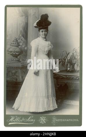 Original late Victorian or early Edwardian cabinet card of fashionable, elegant, attractive beautiful young lady wearing a hat with an ostrich feather, white summer dress. Victorian lady. Edwardian lady. From the studio of Hellis & Sons, London, England, U.K. circa 1901. Stock Photo