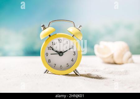 Yellow alarm clock on summer sand sea beach with waves and seashells at background. Time for vacation travel concept. Ten o'clock Stock Photo