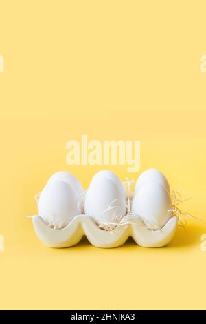 Organic white chicken eggs in porcelain decorative box on yellow background for Easter egg dyeing. Natural healthy food. Vertical greeting card with c Stock Photo