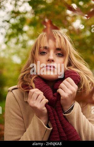 Portrait of young blonde woman wearing a scarf with autumn background and leaves