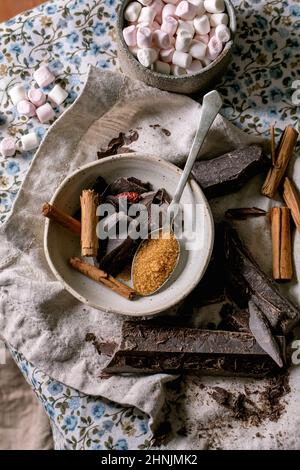 Ingredients for make hot chocolate winter drink in bowl. Chopped dark chocolate, species, cane sugar, marshmallows on rustic linen tablecloth in count Stock Photo