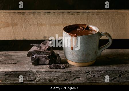 Ceramic cup of hot spicy homemade chocolate winter drink with chopped dark chocolate bar on old wooden shelf. Warm cozy drink. Stock Photo