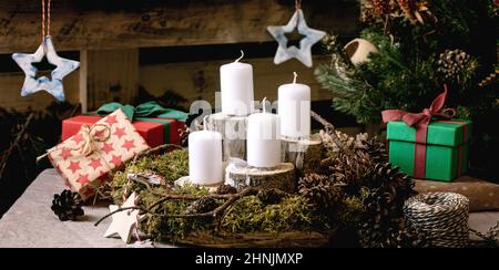 Christmas fashion rustic style interior decor. DIY natural moss wreath and Advent candles on table. Craft ceramics and gift boxes on wooden pallet as Stock Photo