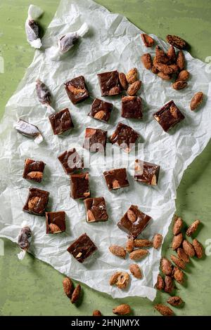 Homemade toffee salted caramel chocolate almond nuts candy on crumpled paper over green background. Handmade food sweet gifts for any holidays. Top vi Stock Photo