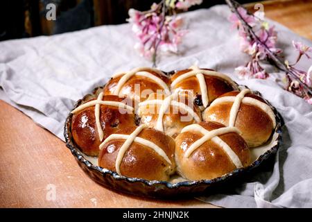 Homemade Easter traditional hot cross buns on ceramic dish with blossom flowers over orange stone table with linen cloth. Easter holiday baking Stock Photo