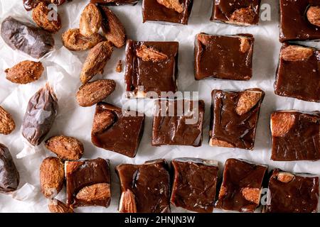 Homemade toffee salted caramel chocolate almond nuts candy on crumpled paper in row over white linen tablecloth. Handmade food sweet gifts for any hol Stock Photo