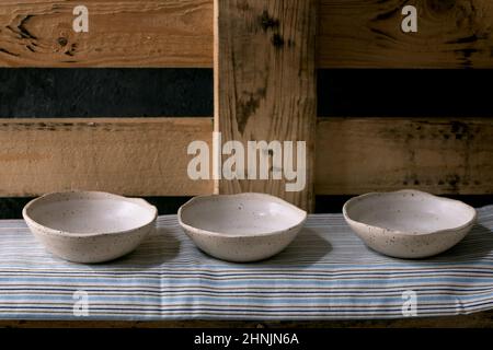 Set of empty craft ceramic white speckled bowls in row standing on wooden shelf. Stock Photo