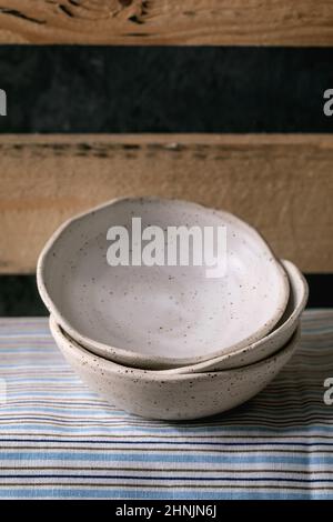 Set of empty craft ceramic white speckled bowls in stack standing on wooden shelf. Stock Photo
