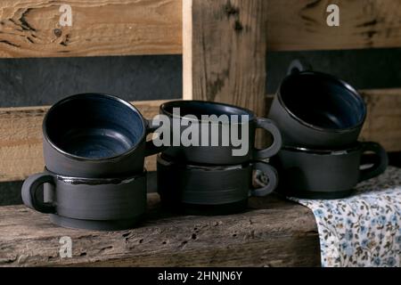 Set of empty black matt craft ceramic coffee tea cups standing on wooden shelf. Rustic interior Stock Photo