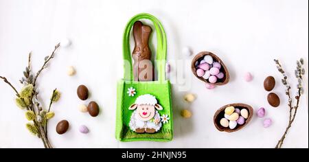 Easter greeting card with chocolate sweets rabbit in green bag, candies and eggs, willow branches on white background. Easter treats, banner size Stock Photo