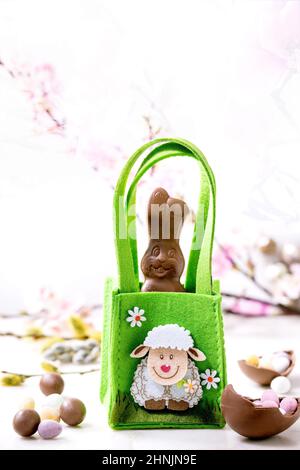 Easter greeting card with chocolate sweets rabbit in green bag, candies and eggs, willow branches and spring flowers on white background. Easter treat Stock Photo