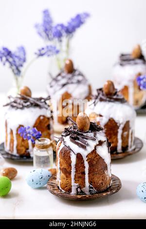 Homemade traditionla small Easter kulich cakes with chocolate nests and eggs on plates decorated with muscari flowers over white background. Tradition Stock Photo