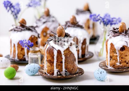 Homemade traditionla small Easter kulich cakes with chocolate nests and eggs on plates decorated with muscari flowers over white background. Tradition Stock Photo
