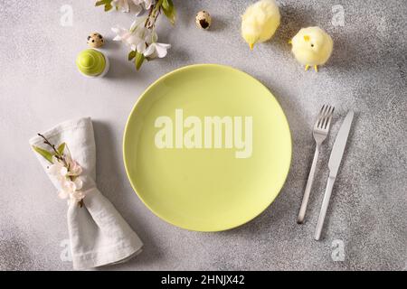 Easter table setting with green plate, spring blossom flowers and green eggs on gray background. View from above. Space for text. Stock Photo