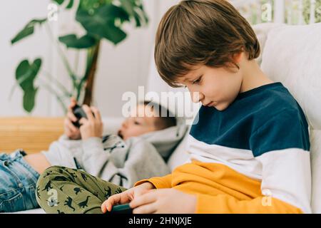 Cheerful two Childs boys playing online game, watching video on cellphone. Smiling kids using funny mobile apps, enjoying free leisure time at home on Stock Photo