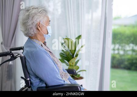 An elderly woman sitting on wheelchair looking out the window for waiting someone. Sadly, melancholy and depressed. Stock Photo