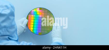 Engineer in clear room in white gloves and suit holding a silicon wafer with integrated circuits on a white background. Stock Photo