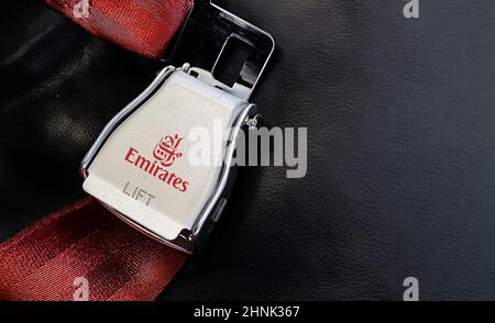 Red lap belt of an empty seat inside an airplane with the Emirates logo printed on the metal. Stock Photo
