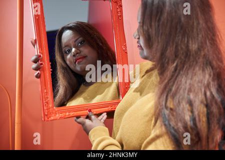 Beautiful African-American woman looking into a mirror thoughtfully. Stock Photo