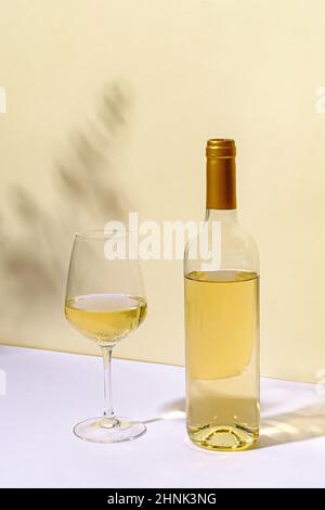 Unlabelled bottled of white wine with half empty wineglass standing on a white table against a neutral wall with copyspace Stock Photo
