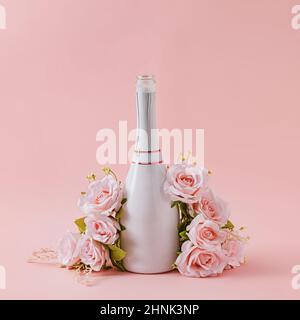 White bottle of champagne with garland of pink roses over a matching pink background with copy space for your greeting Stock Photo