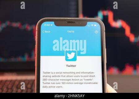 Twitter stock price decrease on the trading market with downtrend line graph bar chart on the background. Man holding a mobile phone with company logo, February 2022, San Francisco, USA.  Stock Photo