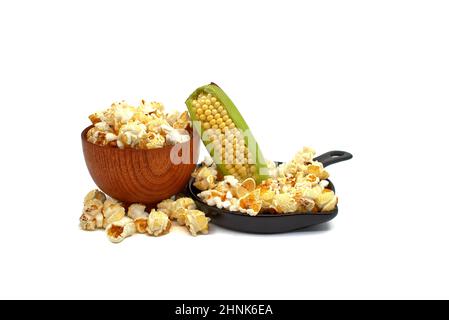 Fresh corn on the cob with bowls of popcorn snack spilling onto a white background in a diet and nutrition concept Stock Photo