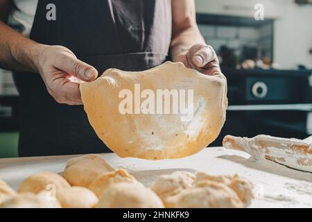 muscular hands of male baker hold thinly rolled dough. Cooking in home kitchen dough for pizza or pita bread. man prepares homemade cakes Stock Photo