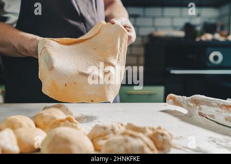 muscular hands of male baker hold thinly rolled dough. Cooking in home kitchen dough for pizza or pita bread. man prepares homemade cakes Stock Photo