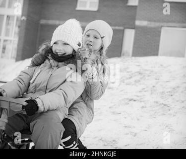 two young girls sledding together and smile Stock Photo