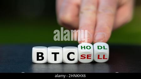 Symbol for keeping (hodl) Bitcoins (BTC). Hand turns dice and changes the expression "BTC sell" to "BTC hodl". Stock Photo