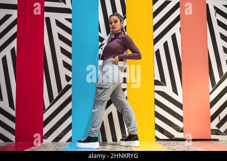 Young woman standing and posing sideways while looking at camera against an abstract wall Stock Photo