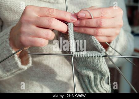 Female hands hold knitting needles and knit a sock. Handmade and hobby concept. Close-up. Stock Photo