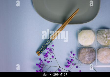 Traditional Japanese dessert mochi in rice dough or daifuku. Mochi ice cream balls and gray plate, food chopsticks on blue background flatly. Table se Stock Photo