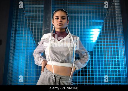 Young woman posing with her hands on her waist while looking at camera with a blue light on background Stock Photo