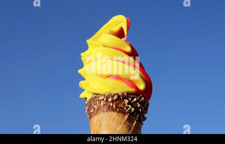 Colorful Pineapple and Raspberry Flavored Soft Serve Ice Cream Cone on Vivid Blue Sky Stock Photo