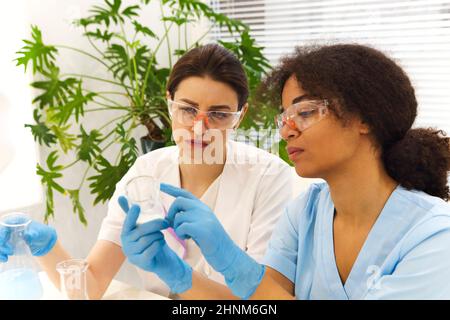 COVID-19 Testing Lab. Two women medical laboratory scientists colleagues wearing glasses working with test tubes, multi-ethnic graduate students worki Stock Photo