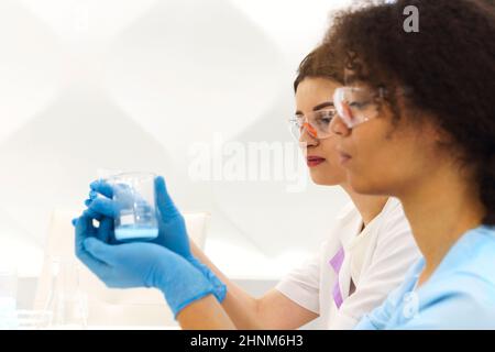 COVID-19 Testing Lab. Two women medical laboratory scientists colleagues wearing glasses working with test tubes, multi-ethnic graduate students worki Stock Photo