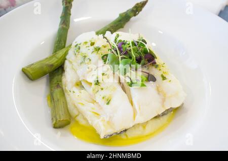 Oven-roasted codfish topped with green wild asparagus and corn salad. Closeup Stock Photo