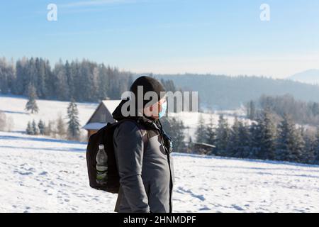 Senior man wearing protective mask due to the Covid-19 coronovirus pandemic, walking in the mountains in winter, Gorce National Park, Poland. Stock Photo