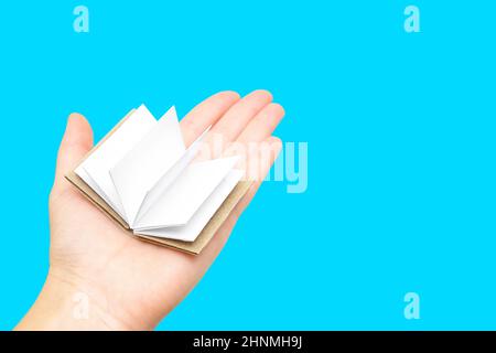 Miniature open book with blank pages on the palm of the female hand against a blue background. Stock Photo