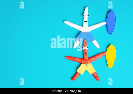 Two funny starfish characters with surfboards lying on a blue background imitating water. Creative surfing vacation concept. Stock Photo