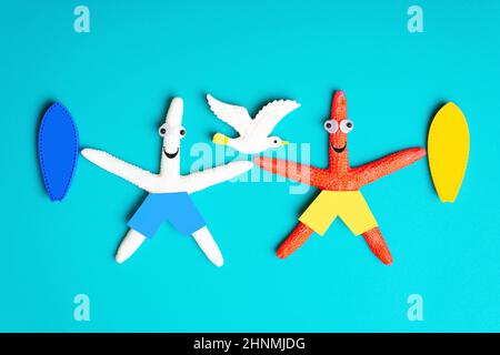 Two funny starfish characters with surfboards and a white seagull isolated on a blue background. Creative surfing trip concept. Stock Photo