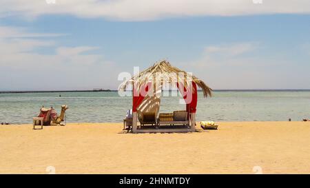 Luxurious Arabian-style straw tents on the Red Sea and camel in the Egyptian resort of Sharm El Sheikh. Summer beach concept, design for relaxation and tranquility. Stock Photo