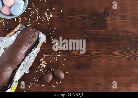 Easter eggs and chocolate bunny on dark wooden background with yellow flower decorations. Top view. Copy space. Stock Photo