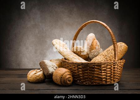 assortment of baked bread in wicker basket on wooden table Stock Photo