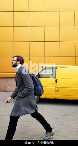 Ukraine, Kiev - February 25, 2020: a mature male businessman in a hurry to meet or work in a gray coat on a yellow background. Casual style. fashionable man with a beard. Male fashion model. Stock Photo