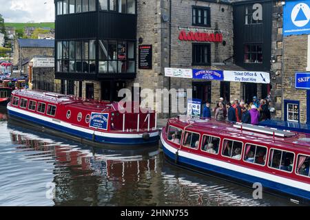 Busy popular tourist leisure experience (red boat moorings, men women queuing waiting by water) - scenic Leeds-Liverpool Canal, Yorkshire, England UK. Stock Photo